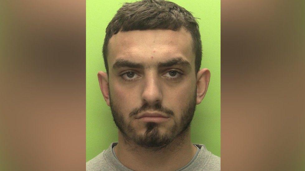 A mug shot of Connor Copse wearing a grey jumper on a green background