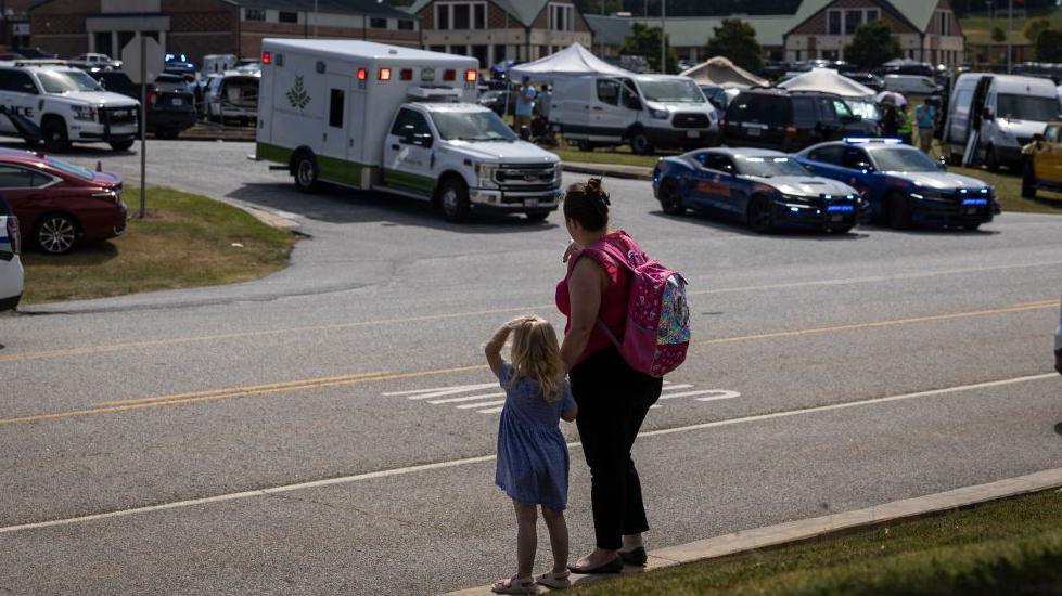 A parent and young child watch as an ambulance goes by