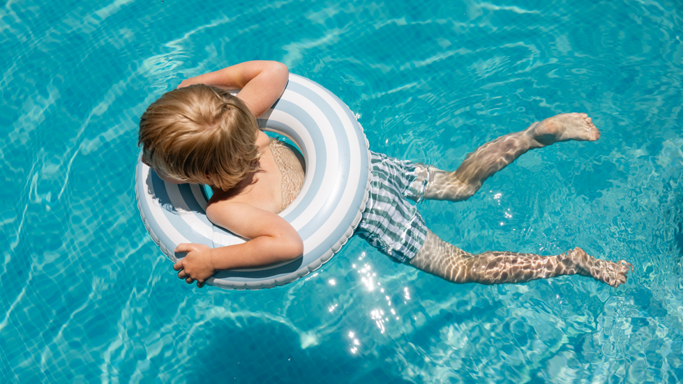 A child swimming in crystal blue water, he is in the middle of an inflatable ring.