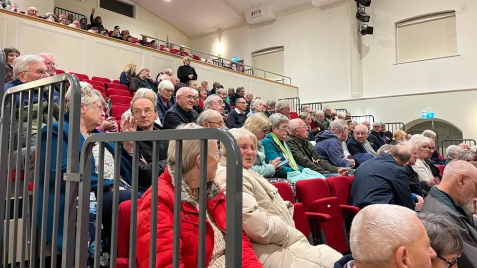 People in tiered seating at a public meeting