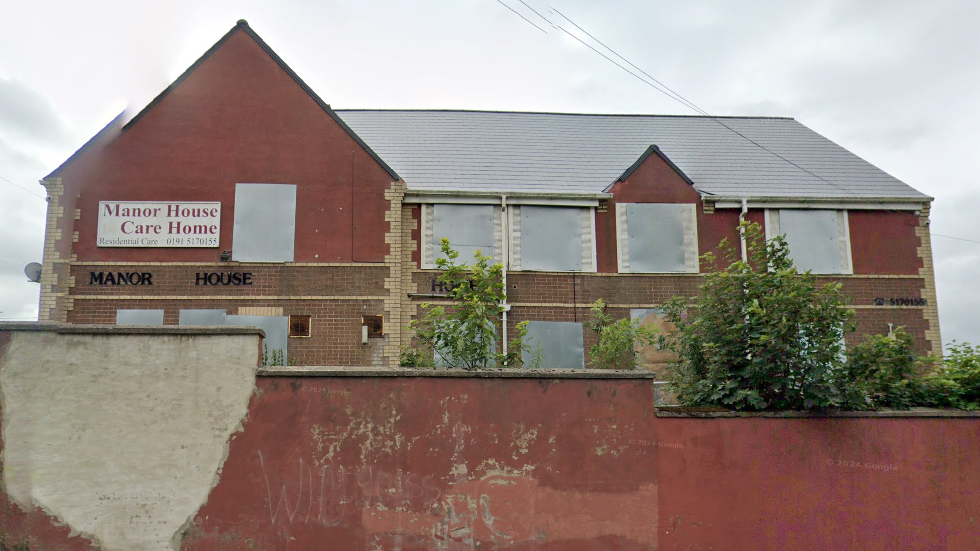 A street view of Manor House which is a large, red brick building with boarded up windows. A Manor House Care Home sign is on the front of the building.