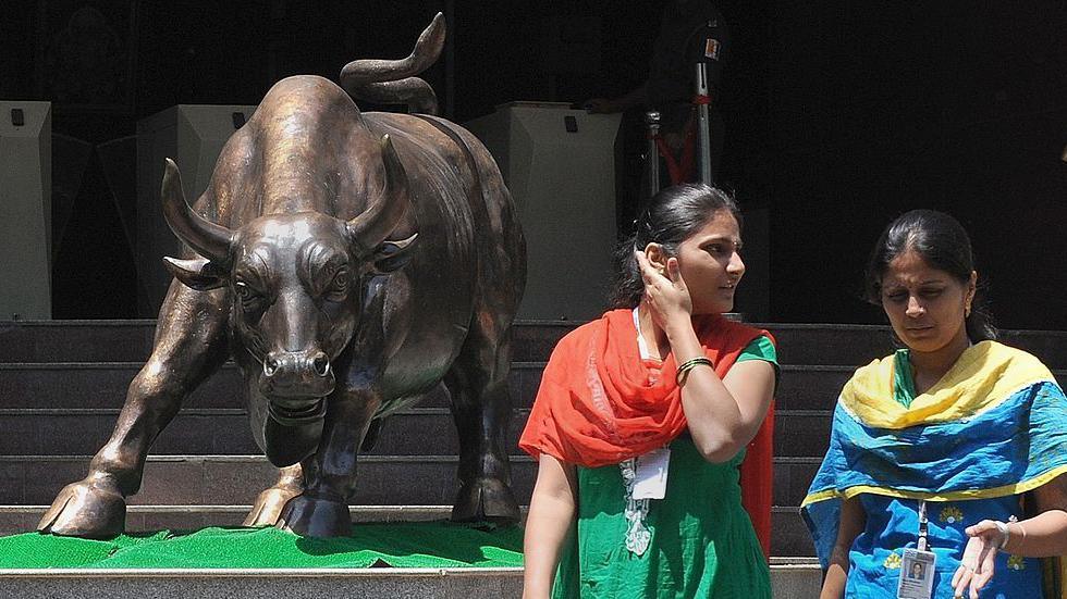 Indian women walk past the bronze bull outside the Bombay Stock Exchange, wearing traditional salwar-kurtas.