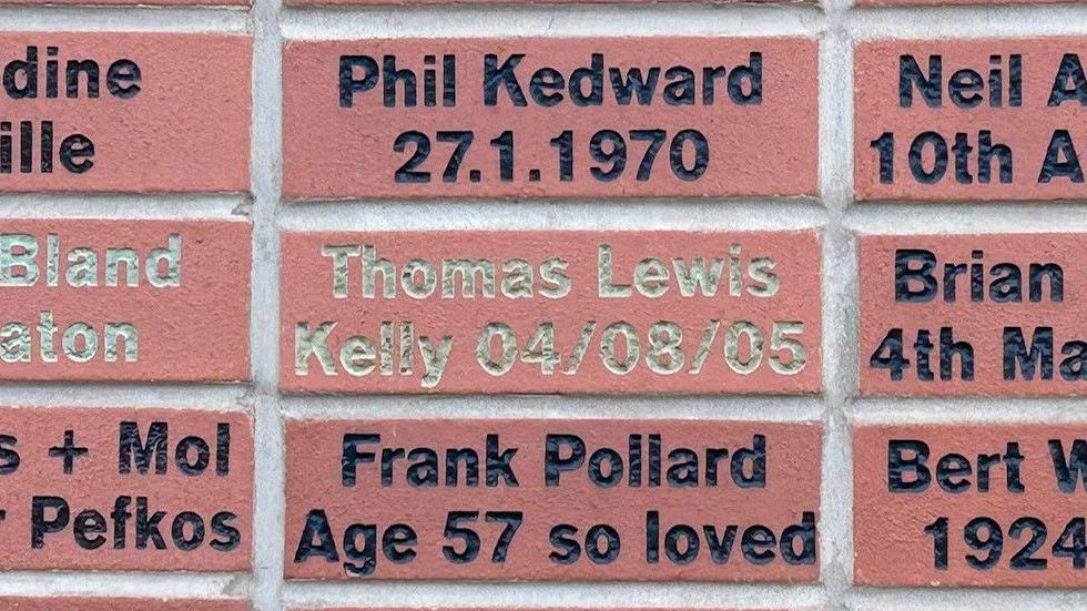 Dozens of bricks with names, messages and birth dates. In the middle is one in grey writing with "Thomas Lewis Kelly 04/08/05" written on it.
