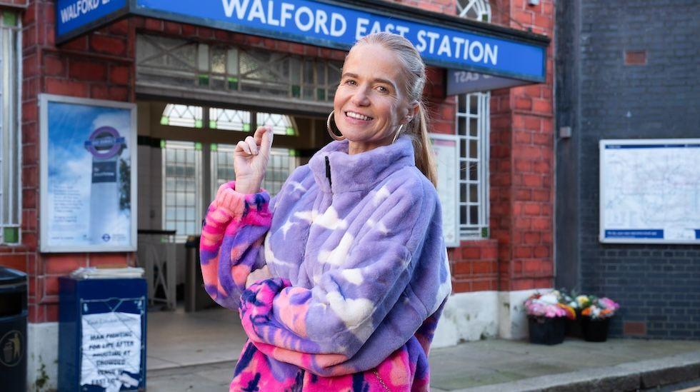 Patsy Palmer appears as Bianca Jackson, wearing a pink and purple fleece outside Walford East Station.