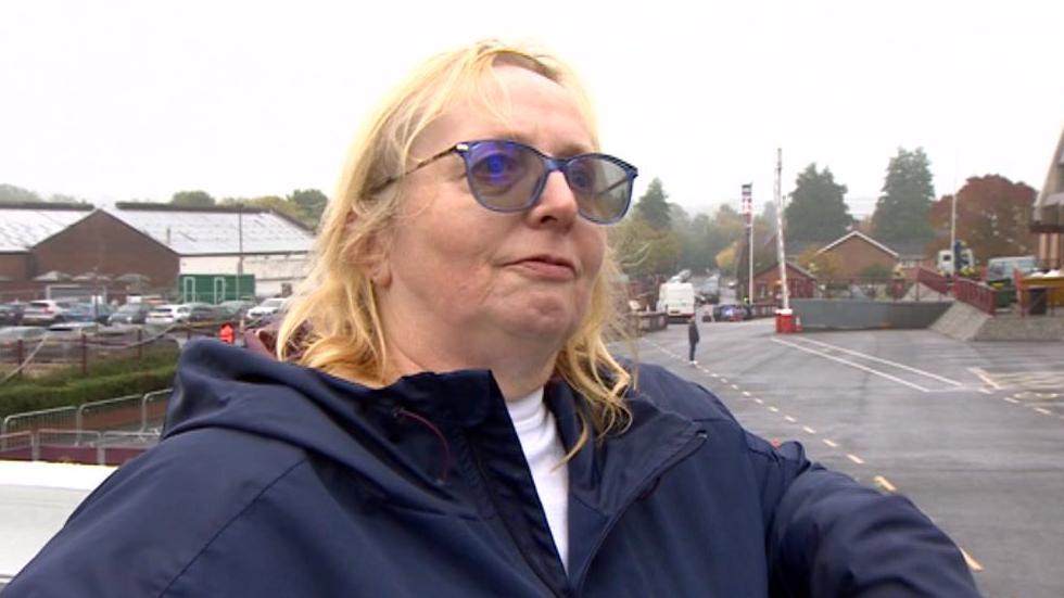 Lynne Wilson - a woman with long blonde hair, dark glasses and a blue jacket - looks to her left as she's being interviewed.