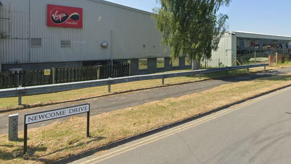 A view of the Newcome Drive street sign with some of the road and an industrial building behind
