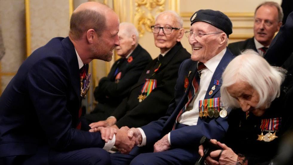 Prince William smiles as he chats with veterans at a reception for veterans who served in the Pacific during World War Two, part of the commemorations marking the 80th anniversary of VJ Day, at Windsor Castle. The veterans feature wear their military service medals on dark jackets.