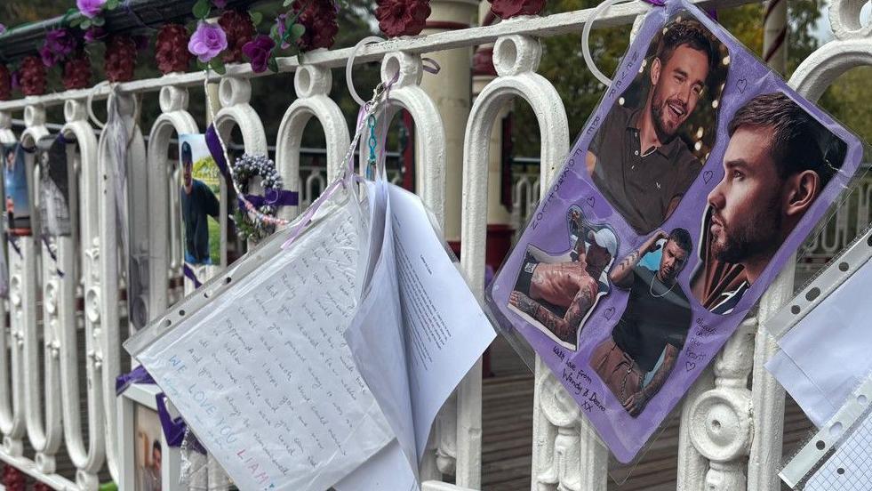 Picture tributes are on the right of this photo attached to railings. Other tributes are also attached on the middle and left of this image.