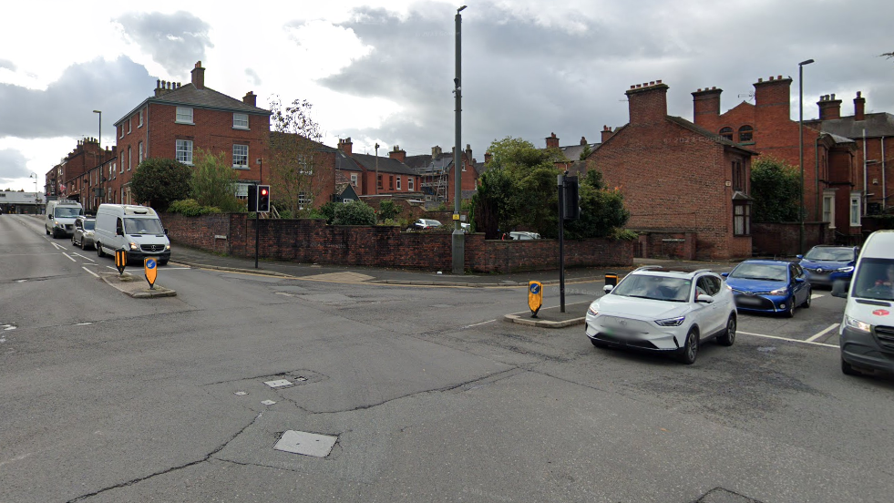 A four-way junction that has cars waiting at two entrances. There are potholes and dents in the road.