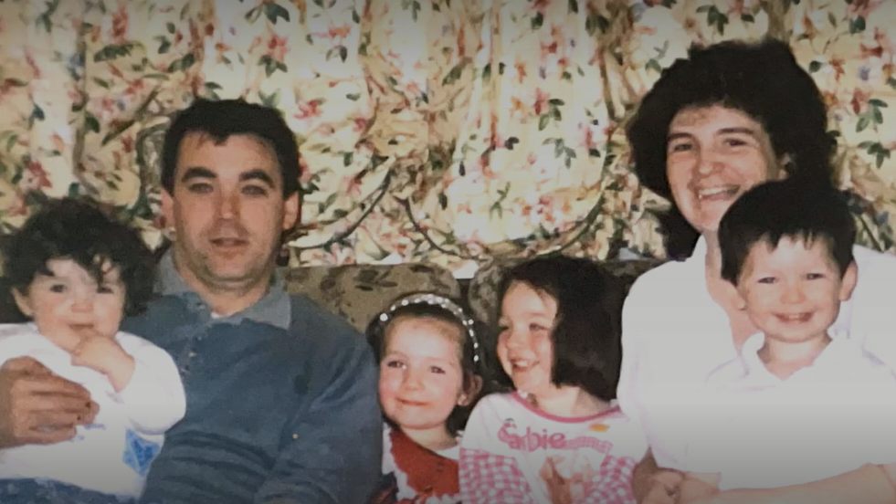 Maura and her husband with their four children, a boy and three girls, sitting on a sofa