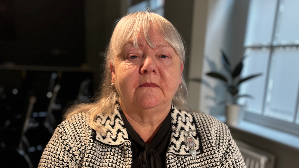 Norma Southern with wearing a black and white dogtooth print cardigan, facing the camera. 