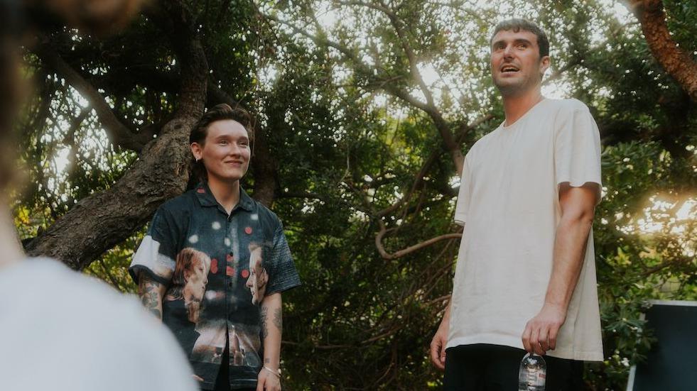 SOAK in a patterned green shirt, Fred Again in a white t-shirt, pictured in front of greenery in Greece