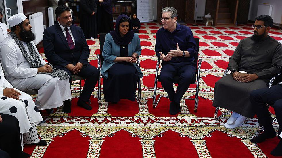 A group of people sitting on chairs, in a circle, inside a mosque.