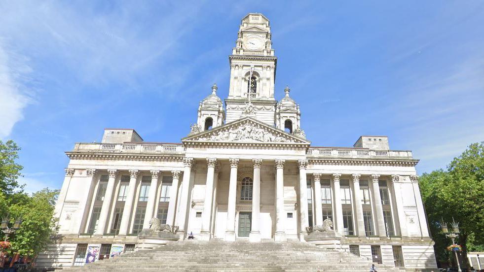 A Google Street View of Portsmouth Guildhall, a large white building with large columns in the Ancient Greek style.