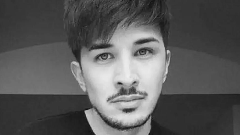 Black and white image of the late Martyn Hett, one of the victims of the Manchester. He has black hair and stubble wearing a black top. 