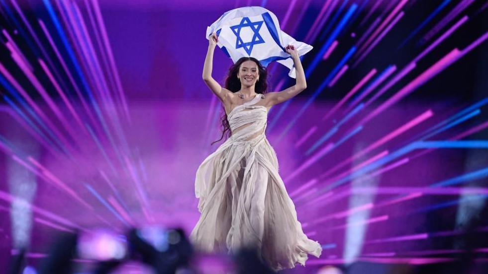 Eden Golan representing Israel holds the flag of Israel on stage at the Eurovision Song Contest in 2024