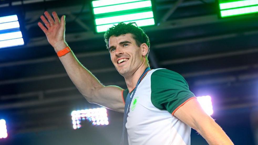 Rower Philip Doyle, wearing an Ireland top and with his medal around his neck, waves to the spectators at Monday's homecoming event