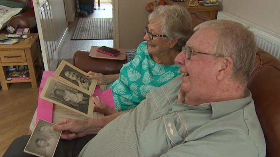 Michael Hamson, 79, and sister Judith Tomblin, 86. They are sat on a couch in a living room looking through old photographs. 
