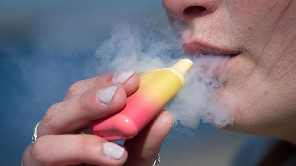 A close up of a person smoking from a pink and yellow disposable vape