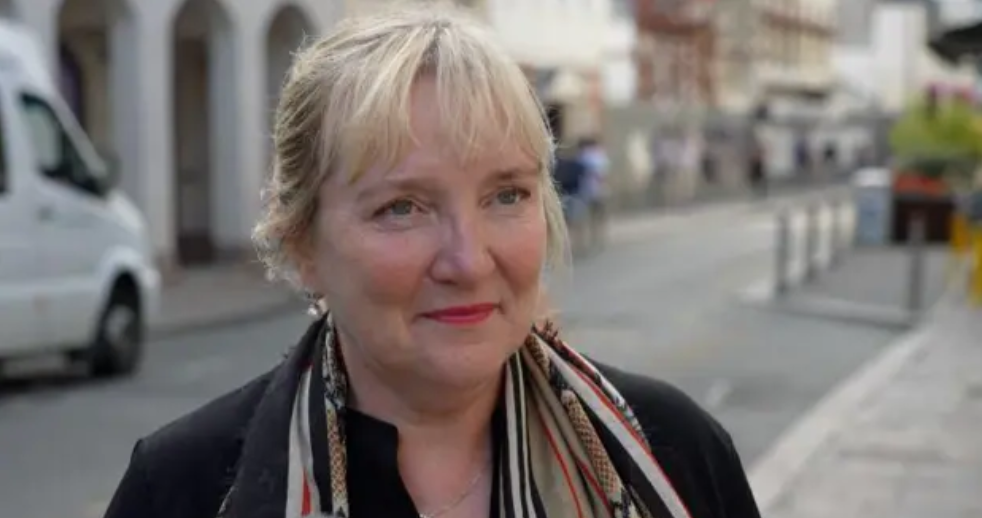 Tricia Warwick smiling at the camera, wearing a black jacket and scarf. 