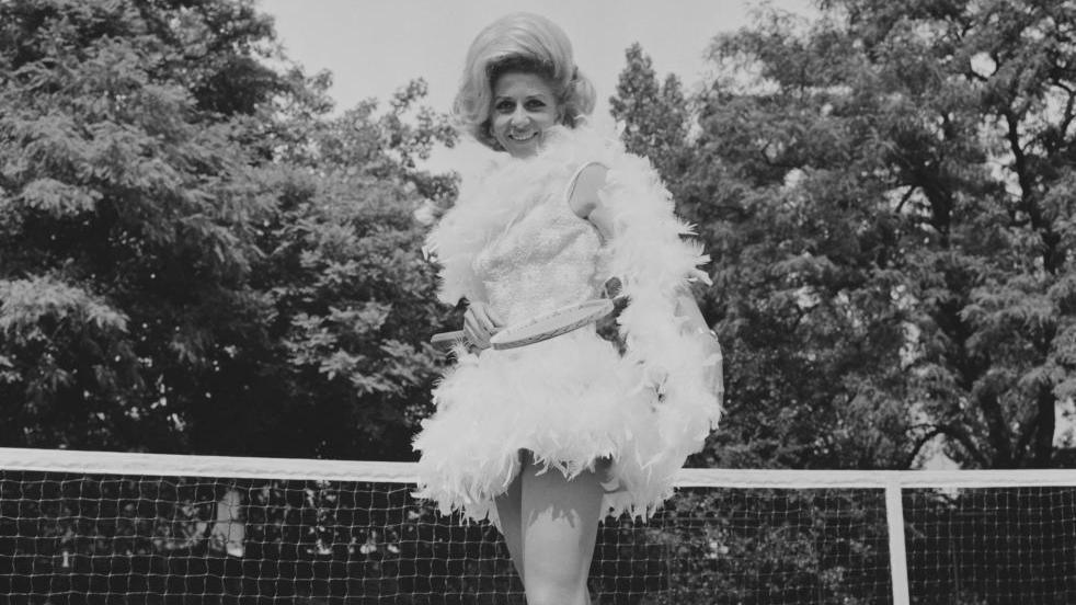 Pericoli is seen standing in front of a tennis net, posing in a feathered outfit on court in the UK, 23rd June 1968.