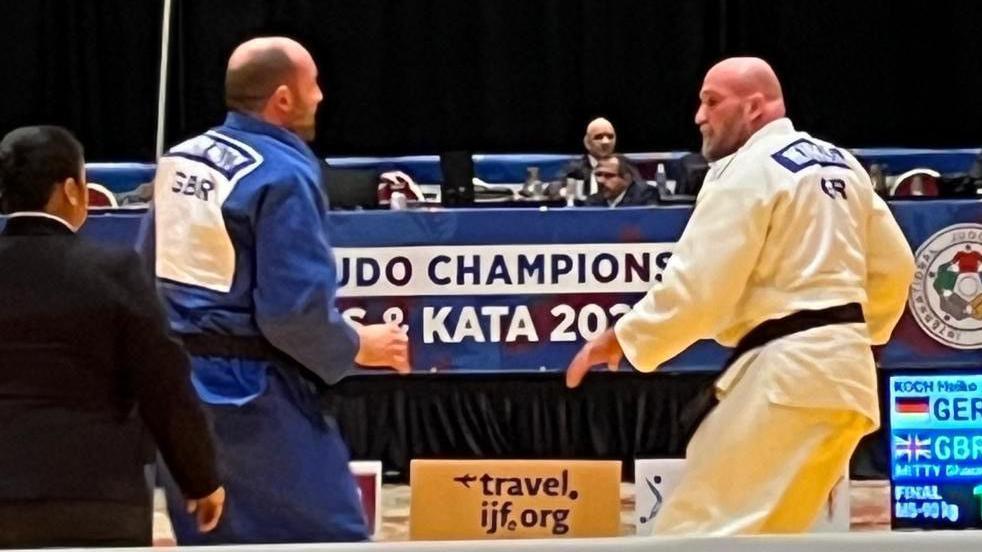 Action shot of a fight between two men. One is wearing a white judo uniform and the other is wearing blue