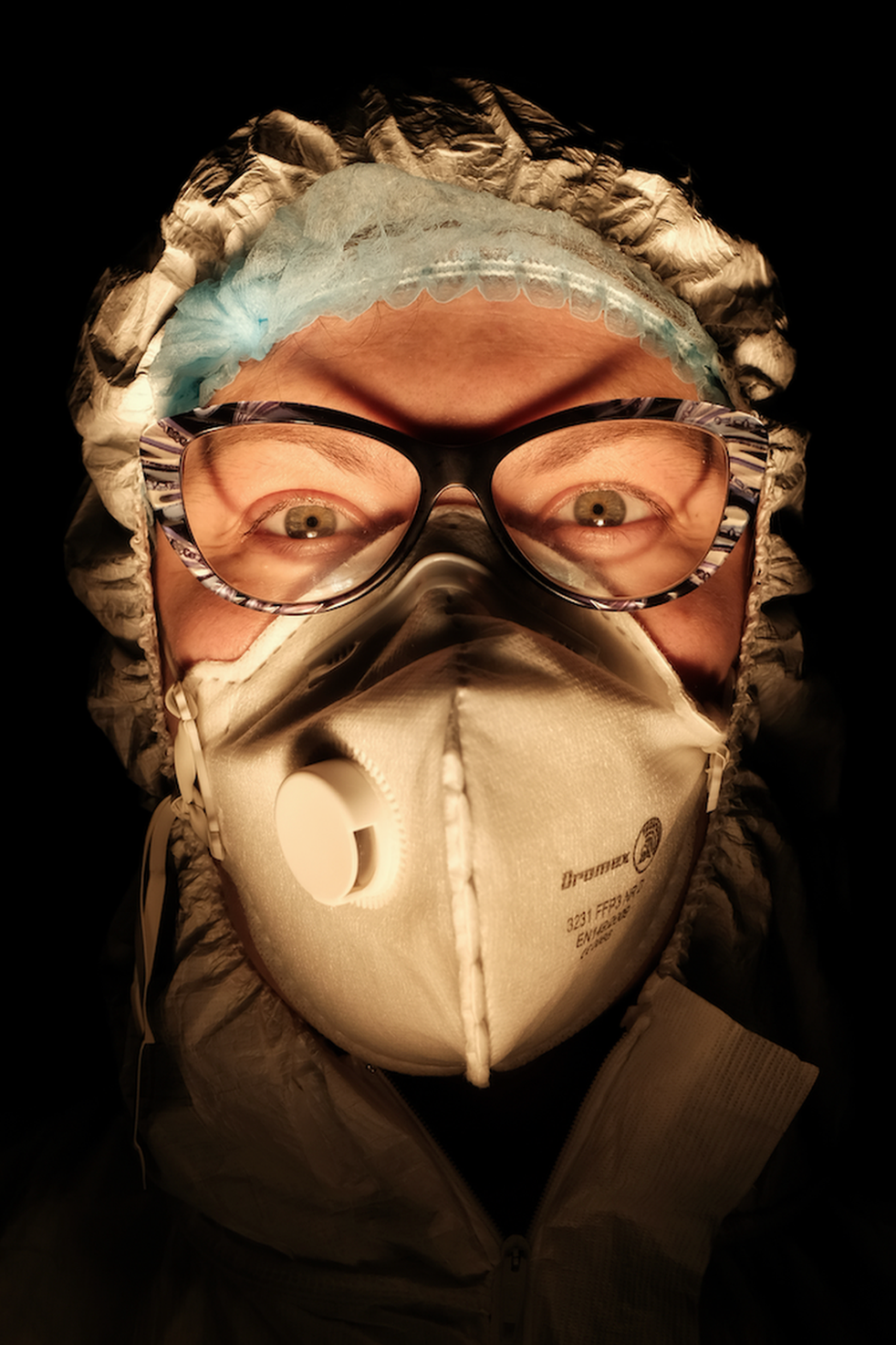 A female nurse wearing a face mask with a dark background behind her