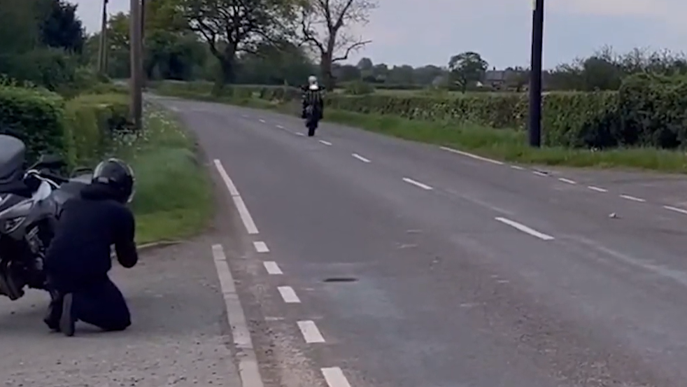 A still from the footage shows Benjamin Males doing a wheelie as he rides on a rural road. Another biker is in a driveway as he goes past.