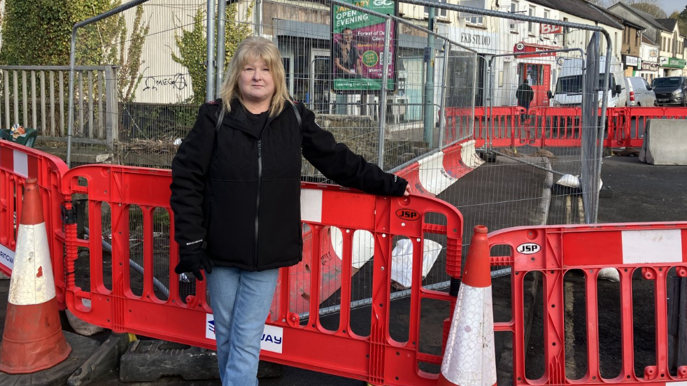 Photo of Lydney resident Karal Smith standing in front of a closed bridge, with red and white closure barriers behind her and red and white traffic cones