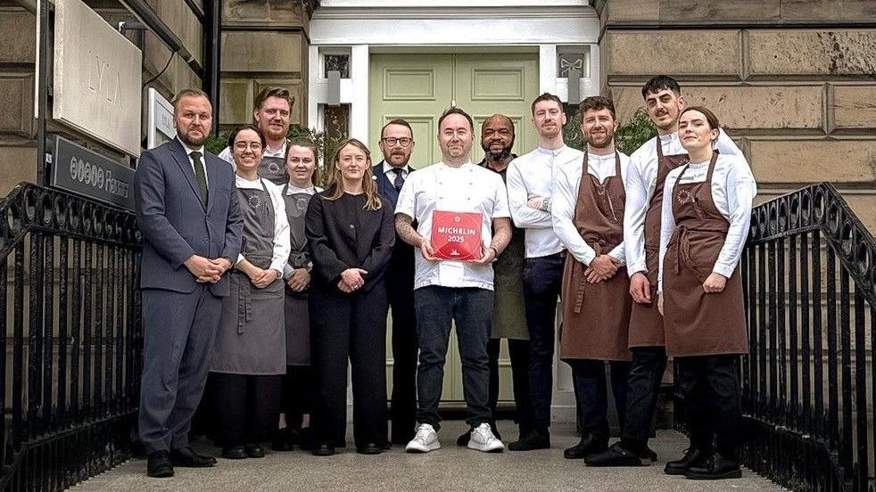 Stuart Ralston and his Lyla staff gathered outside the restaurant, a Georgian mansion in Edinburgh, in their aprons and chef's whites, with Stuart in the centre holding the red Michelin plaque.