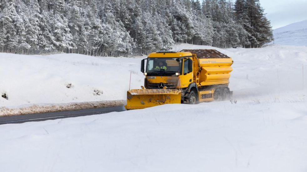 A bright yellow snowplough makes its way through heavy snowfall on the A87 road between Inverness and Ullapool
