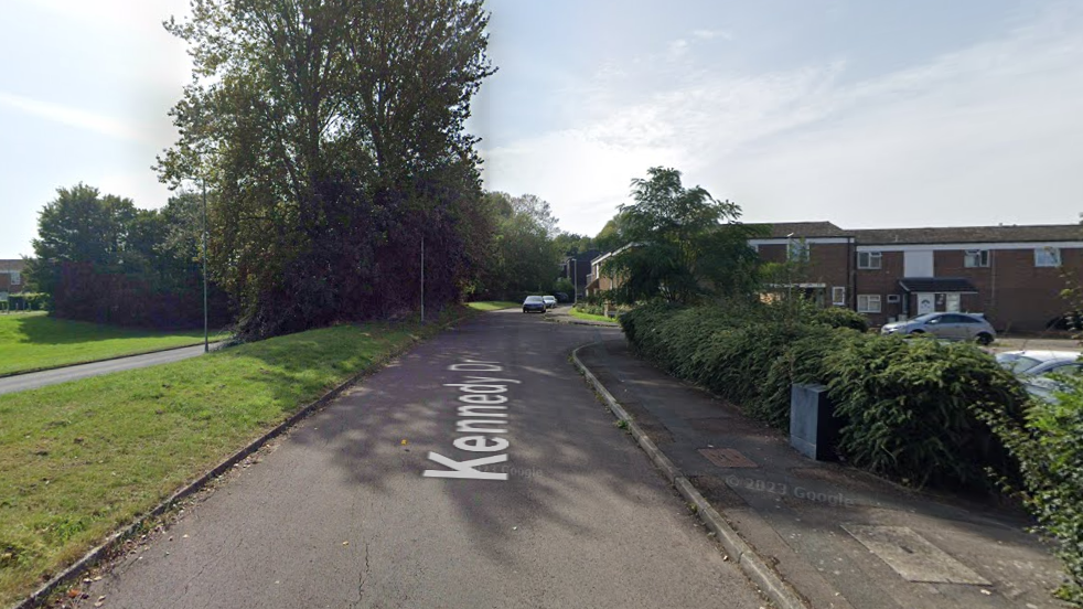 A Google street view image of Kennedy drive - a residential area in Eldene Swindon. There are a number of residential properties and a main road to the left.