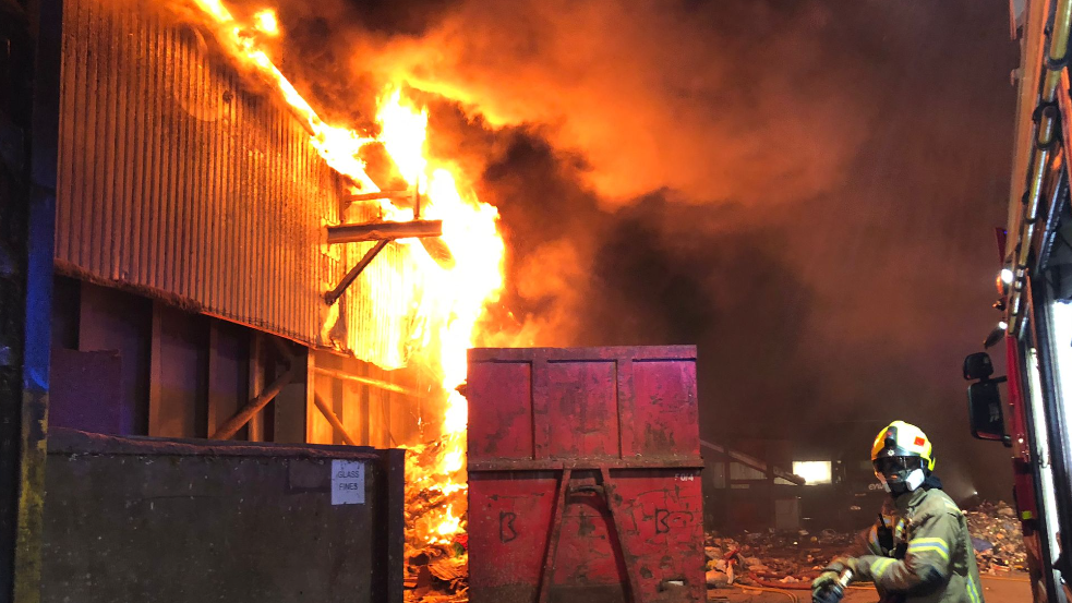 A fire in consuming an industiral building with a firefighter in the foreground