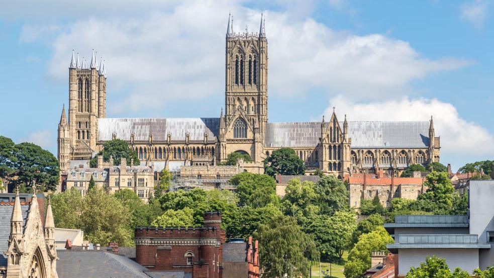 Lincoln Cathedral against a blue sky, with trees and houses in the foreground