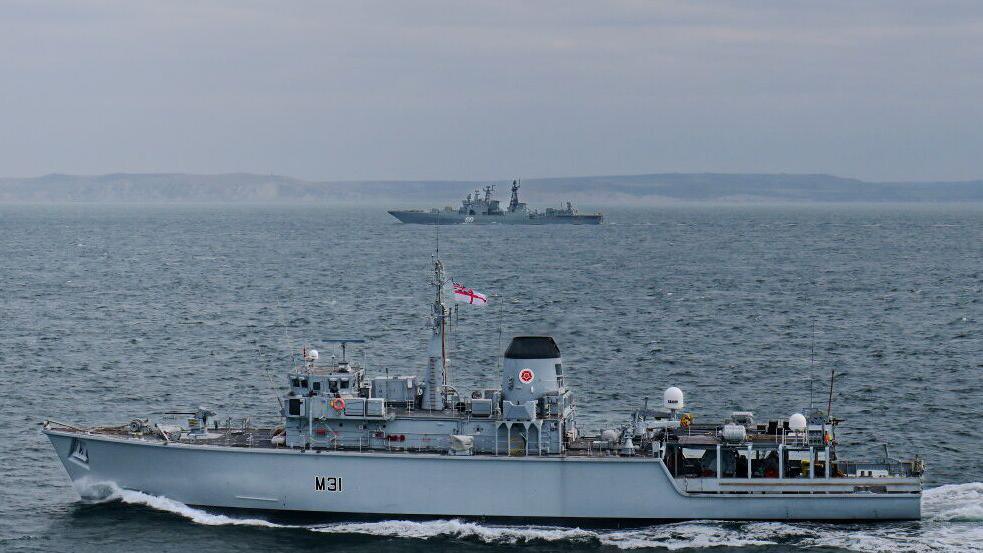 Image shows two ships, in the foreground is Royal Navy vessel HMS Cattistock and in the backround, Russian vessel RFN Severomorsk 619