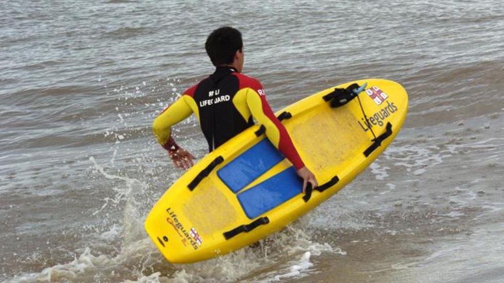 An RNLI Lifeguard walking through the sea holding a lifeguard paddle board