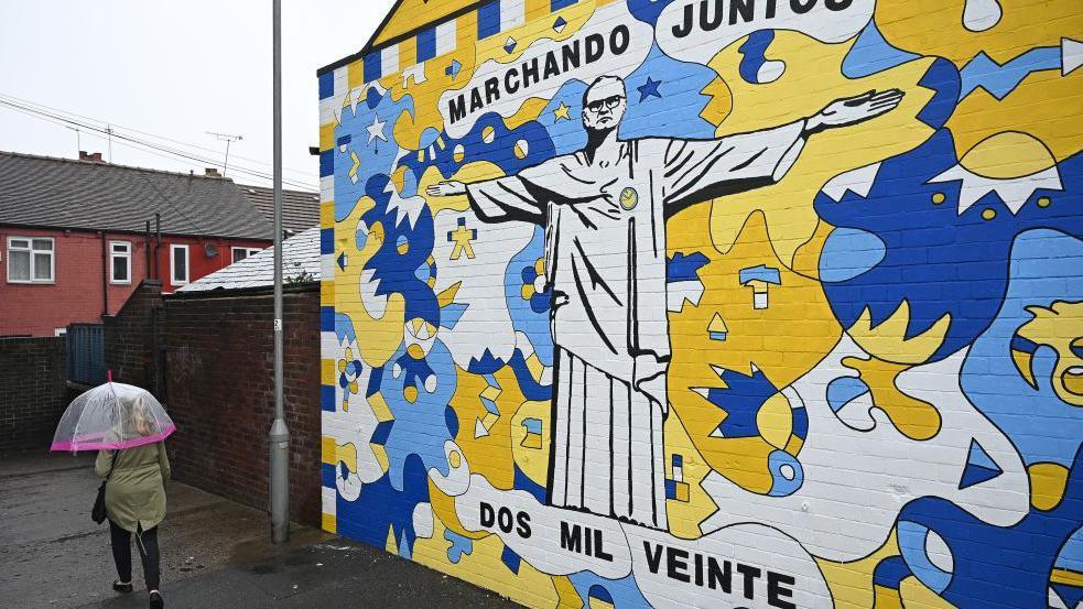 A pedestrian walks past a graffiti mural depicting Leeds United's former head coach Marcelo Bielsa