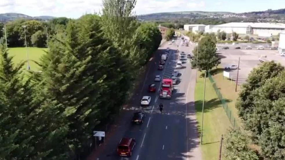 A lorry and cars travelling down a road. It is a shot from above.