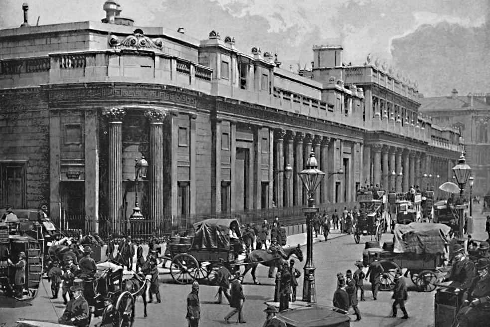 Black and white photo outside the Bank of England in 1896 with people walking on the street along with horse and carts and omnibuses 
