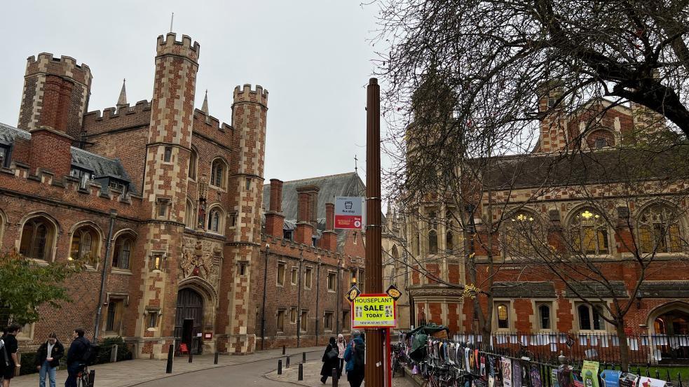 View of St John's Street in Cambridge showing a street light without a lantern at the top. University buildings can be seen in the background and there are pedestrians on the pavements