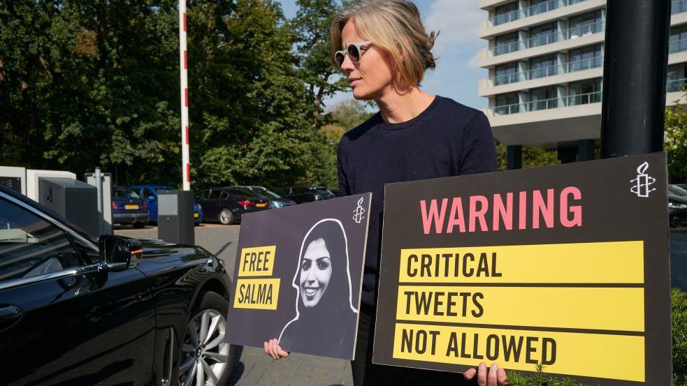 A human rights activist welcomes diplomats with posters criticising the imprisonment of Salma al-Shehab, outside a hotel in The Hague, the Netherlands (22 September 2022)