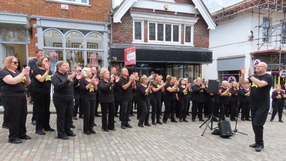 A group of people wearing black standing and clapping their hands while singing.