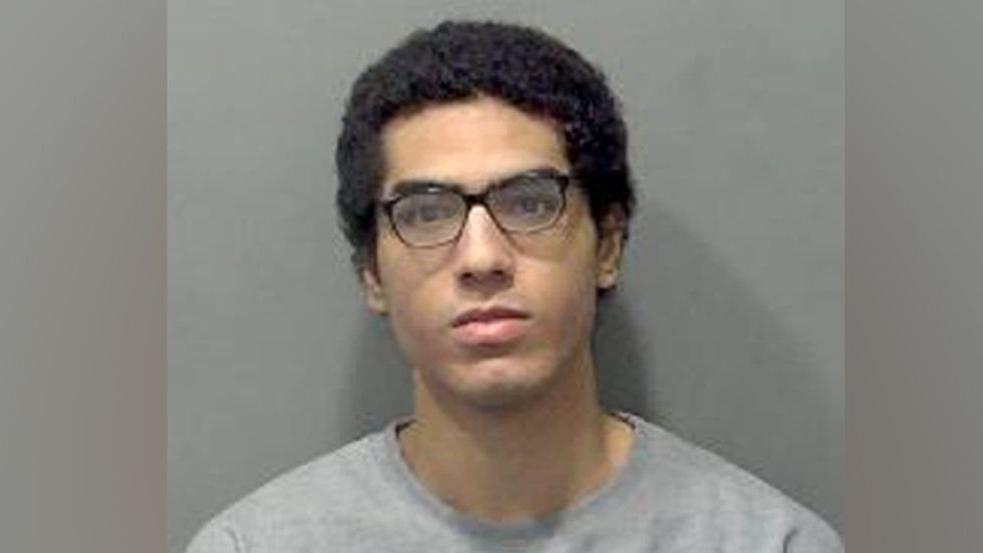 Nicholas Prosper, who has dark hair and dark glasses, staring into the camera for a police custody image. He is wearing a grey sweatshirt.