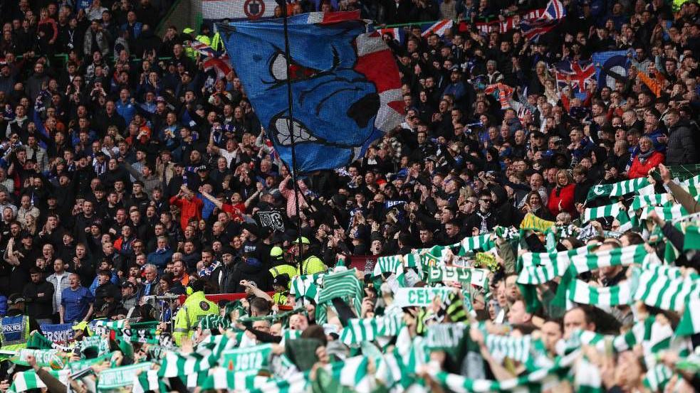 Celtic fans many waving green and white scarfs with a net separating them from Rangers fan many wearing red, white and blue