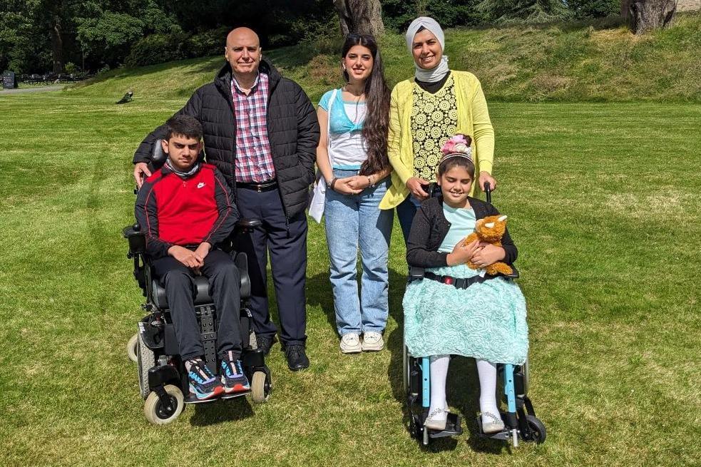 A husband and wife, with a young woman and two children in wheelchairs pose for the camera outside