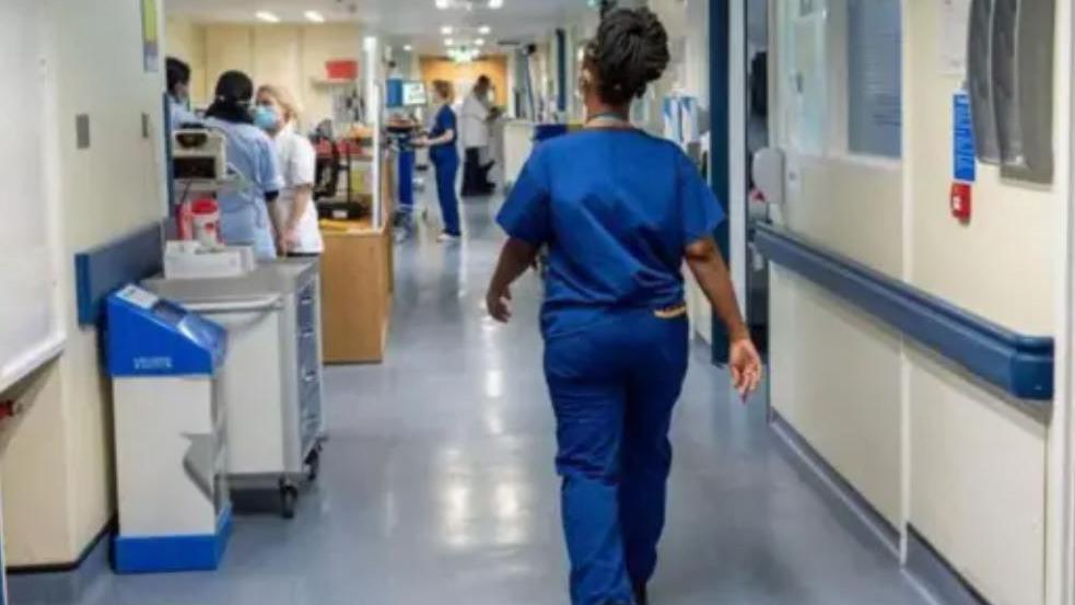 Nurse seen from behind walking along corridor in blue overalls