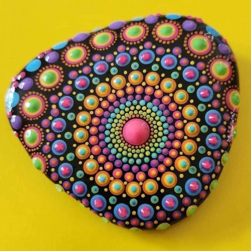 A small rock is painted with multicoloured dots in circular patterns.