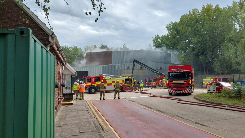 Several fire trucks  and firefighters outside a recycling station tackling an ongoing fire
