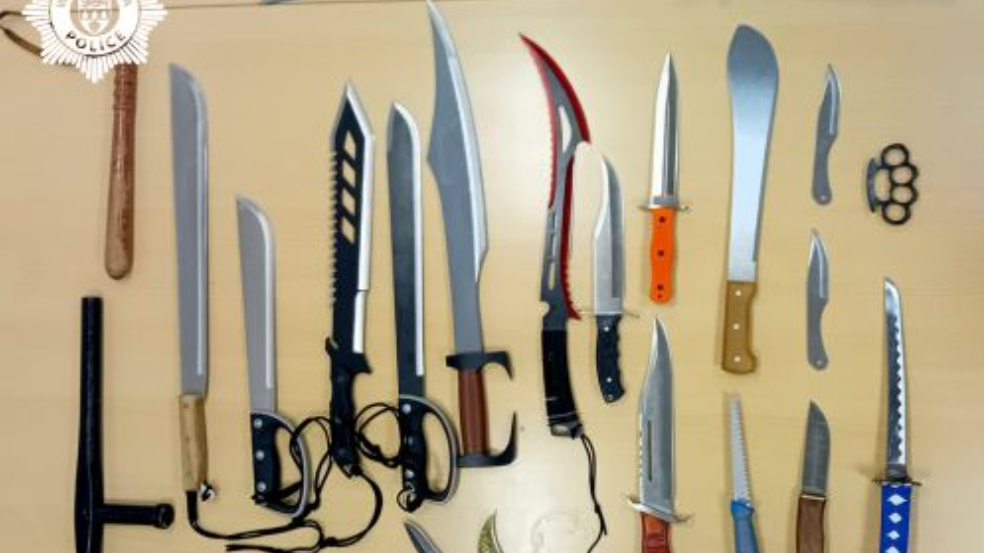 A light brown table with dozens of sharp machetes or zombie style knives