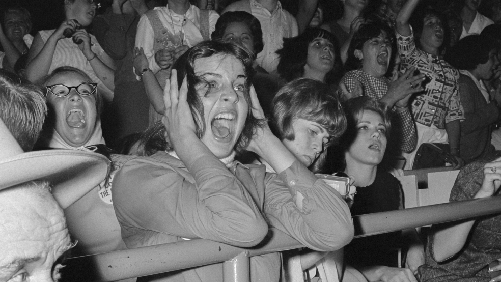 Lots of fans stood behind a metal rail screaming because they have seen The Beatles.